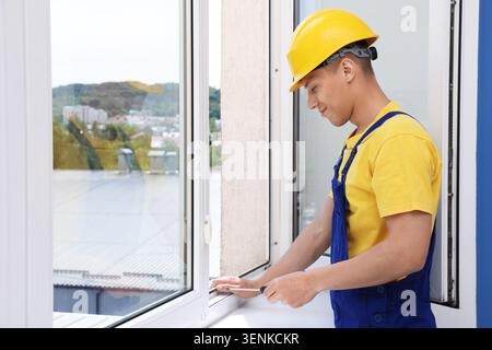 Professional worker with screwdriver installing window indoors Stock Photo