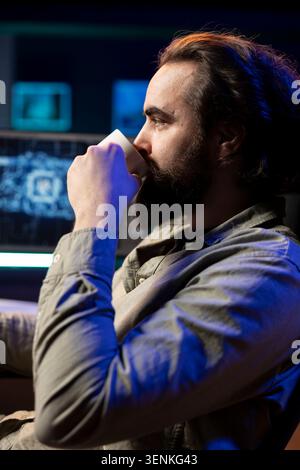 Developer drinking coffee updating artificial intelligence machine learning algorithm on PC desktop at home, IT specialist in apartment office enjoying hot beverage while upgrading AI. Stock Photo