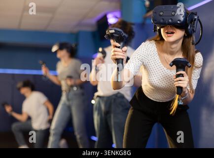 girl in virtual reality helmet crouches down and dodges flying asteroids during space adventure game Stock Photo