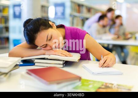Tired woman lying on books at library Stock Photo