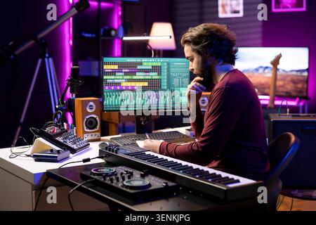 Young producer writing rhymes and words to create new music in home studio, thinking about harmonic notes and elements to compose a beautiful song, with audio engineer produces tunes. Stock Photo