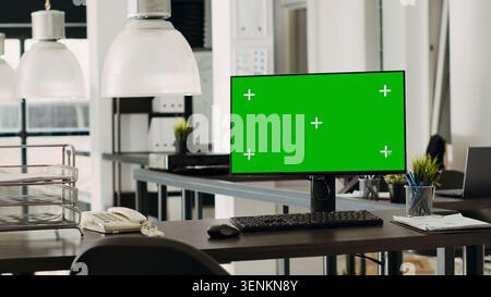 Empty office with green screen on computer display, marketing agency open floor plan. Coworking space with monitor running isolated mockup template, blank chroma key copy space at desk. Stock Photo