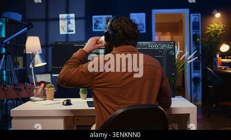Man doing IT support job from apartment office, drinking cup of coffee and listening music while coding. Developer with headphones on enjoying hot tea and writing code on computer, camera B close up. Stock Photo