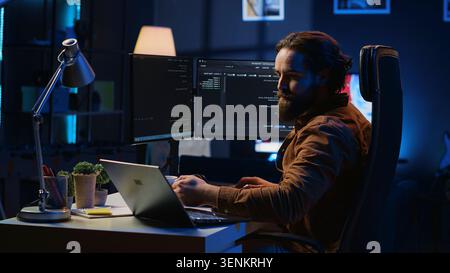 Software programmer putting headphones on while developing code, making time pass faster during remote job shift. Stock Photo
