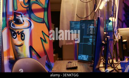 Graffiti painted empty hideaway base with lines of code running on computer screen with malware that get past security systems. PCs in deserted bunker showing scripts that can hack devices. Stock Photo