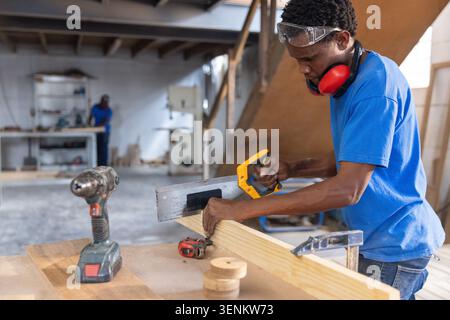 African American coworkers working at workshop bench using handsaw on plank, copy space Stock Photo