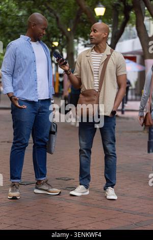 Two adult African American men standing and talking on brick plaza holding smartphone Stock Photo