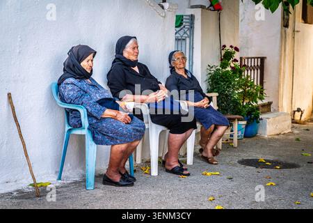 June 24, 2022, Crete, Greece: Three elderly women sitting by a house on a street in the village of Kroustas on Crete, Greece Stock Photo