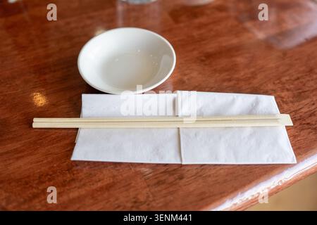 A clean, high-angle, close-up photograph of a simple and elegant place setting in a Japanese restaurant. It features a pair of wooden chopsticks resti Stock Photo