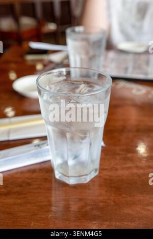 A crisp, close-up photograph of a clear glass filled with cold water and ice cubes, featuring visible condensation on the exterior. The glass rests on Stock Photo