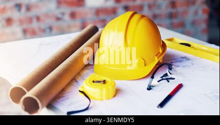 Helmet, construction and tools in empty office for engineering, blueprint design and tape measure. Architecture, equipment or safety ppe at building Stock Photo