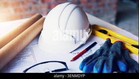Helmet, architecture and tools in empty office with engineering gloves, blueprint or design. Construction, equipment and safety ppe at building site Stock Photo