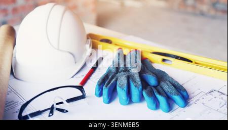 Helmet, architecture and tools in empty office for construction gloves, blueprint or design. Engineering, equipment and safety ppe at building site Stock Photo