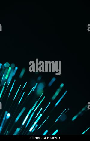 Vibrant turquoise fiber optic lines flare up diagonally from corner against black backdrop Stock Photo