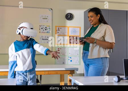 African American teacher and boy engaging in VR lesson at table, teacher holding tablet, copy space Stock Photo