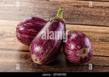 Three striped violet graffiti eggplants resting on rustic wooden table. Fresh raw aubergine with vibrant purple and white streaks, natural lighting, h Stock Photo