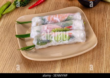 Three fresh vietnamese spring rolls with prawn, vegetables and rice noodles on beige plate, wooden background, healthy asian food, appetizer Stock Photo