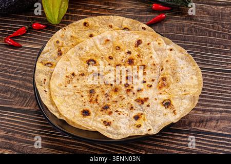 Toasted flatbreads roti surrounded by fresh ingredients. Flat lay with avocado, starfruit, and chili peppers on a rustic dark wood background. Warm fo Stock Photo