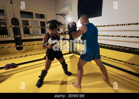 Boxing Training Sparring Session In A Gym Ring With Coach And Female Fighter Practicing Punches Stock Photo