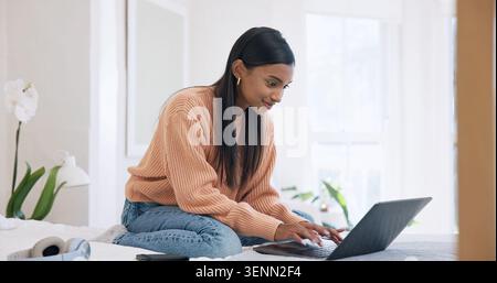 Creative, freelancer and happy woman with laptop on bed, typing and video editing on web in bedroom. Editor, home and Indian person with tech, remote Stock Photo