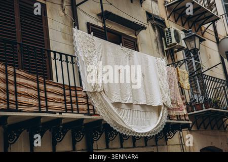 White lace linens drying on a wrought iron balcony of an old building in the historic old town of Palermo Sicily Italy in summer. High quality photo Stock Photo