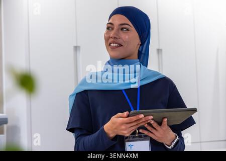 African woman using tablet, checking data in reception cabinets, wearing two-tone hijab, ID badge Stock Photo