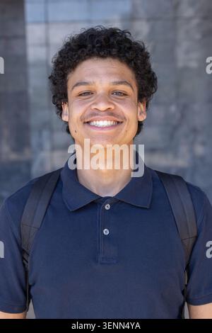 African American man standing in front of mirrored glass smiling broadly wearing navy polo backpack Stock Photo