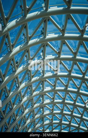 This image captures an abstract, low-angle view of the intricate glass and steel canopy forming the roof of the Bridge of Peace in Tbilisi, Georgia. T Stock Photo