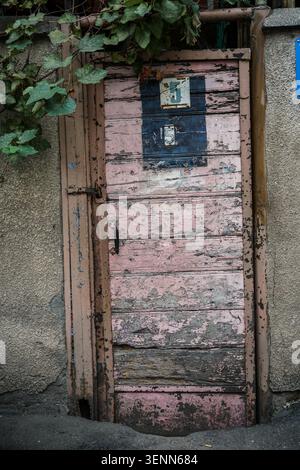 A close-up view of an old, decayed wooden door in Tbilisi, Georgia, featuring peeling pink and dark blue paint. The weathered door shows house numbers Stock Photo