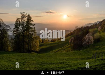Spring sunset over rolling pastures and forested hills near Škofja Loka, Slovenia, with hazy mountain layers beyond. Stock Photo