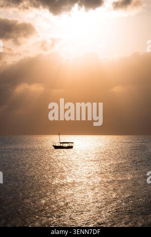 Solitary dhow silhouetted against a golden sunset over the Indian Ocean, Zanzibar, Tanzania, Africa. October 2024. Stock Photo