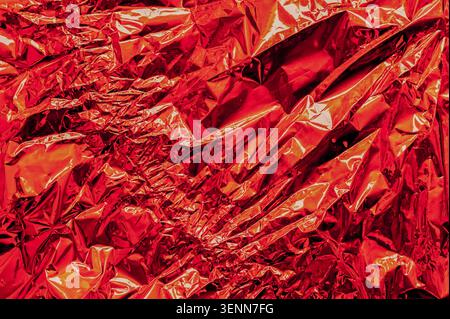 foil texture in red color with crumpled reflective surface and sharp folds, foil forming vivid metallic pattern, bright highlights and deep shadows, a Stock Photo