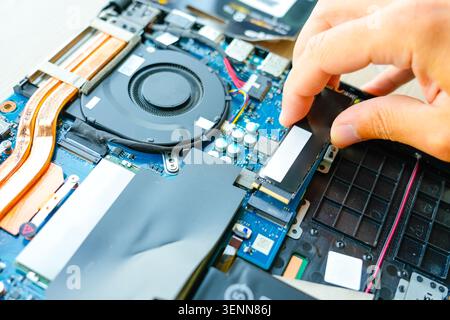 Laptop repair engineer PC computer and motherboard install random access memory ram ssd in computer lab top. The master installs the disk in his hands Stock Photo