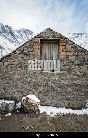An old, weathered stone and concrete building with a rustic wooden window stands in the foreground, its textured walls displaying a mix of materials. Stock Photo
