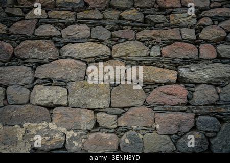 A detailed, full-frame view captures the intricate patterns of a traditional stone wall, constructed from irregularly shaped rocks. The ancient masonr Stock Photo