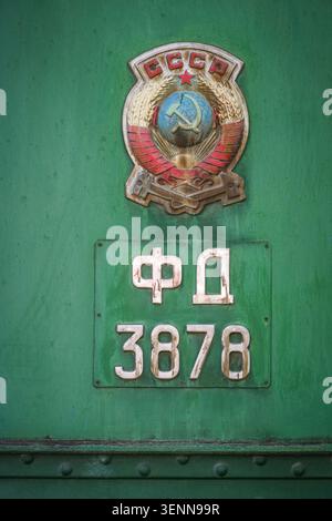 A close-up view of the weathered Soviet Union Coat of Arms emblem and a locomotive nameplate with 'ФД 3878' on a green metal surface. This historic de Stock Photo