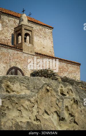 A close-up view of the historic brick bell tower and weathered facade of the Uplistsikhe Church of Prince George, featuring a red tiled roof and cross Stock Photo