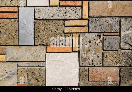 Multicolored external wall made of different types of rocks and bricks arranged geometrically. Background and texture. Stock Photo