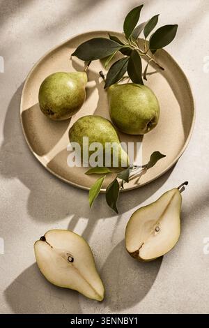 Overhead flat lay shot of three fresh, organic Italian pears with natural green leaves arranged beautifully on a rustic ceramic plate. The plate sits Stock Photo