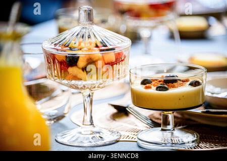 Elegant glass with fresh fruit salad and yogurt with blueberries and granola at an upscale breakfast table. Food styling. Stock Photo