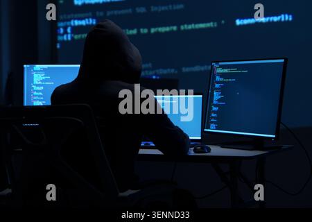 Programmer Hacker Working at Multiple Monitors in Dark Room Stock Photo