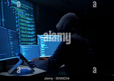 Hacker in Hoodie Working on Multiple Monitors at Night Stock Photo