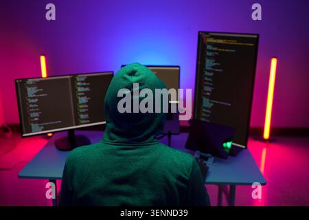 Hooded programmer working at multiple monitors in neon light Stock Photo