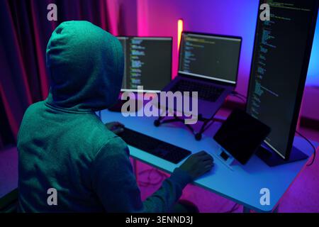Hacker in Hoodie Working at MultiMonitor Coding Setup Stock Photo