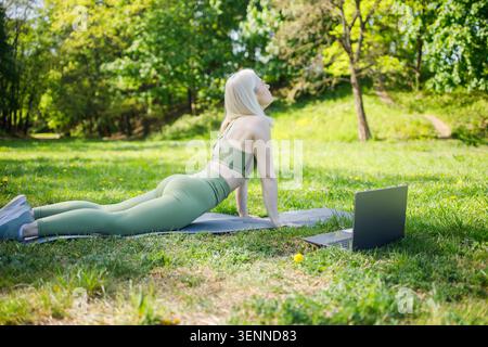 Middleaged blonde woman making stretching exercises outdoors using Stock Photo
