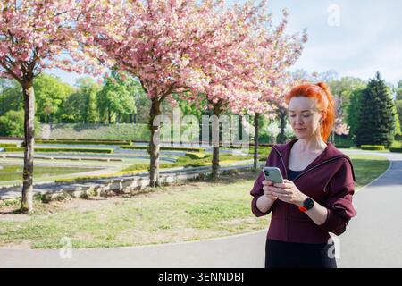 Redhaired middleaged woman using smart phone during morning sport run Stock Photo