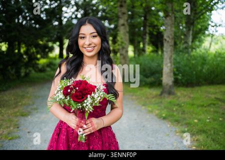 Smiling young woman in red dress holds flower bouquet Stock Photo