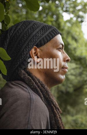 Thoughtful man with dreadlocks standing under a tree Stock Photo
