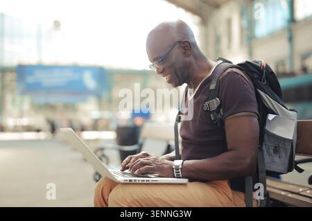 Smiling senior man using laptop at train station Stock Photo