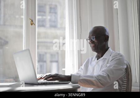 Happy senior Black man using laptop by a window Stock Photo